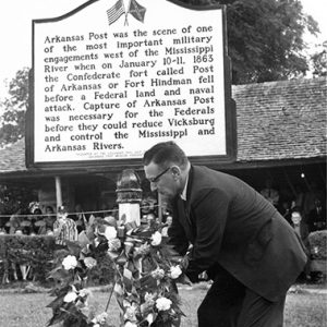 White man placing a wreath under historical marker sign