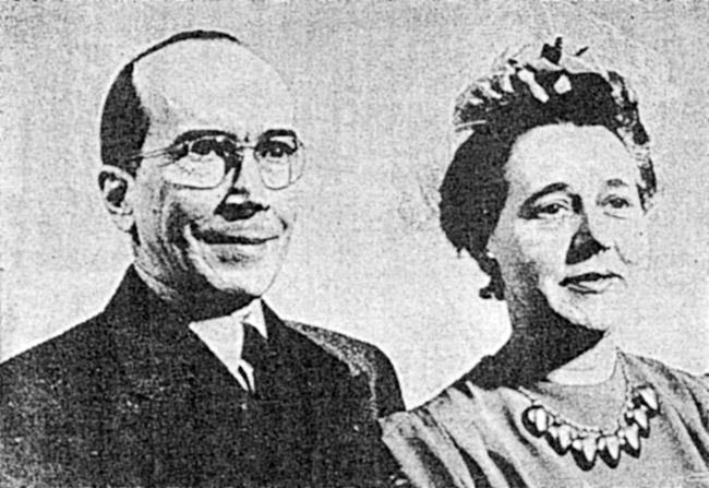 White man in glasses and woman in large necklace smiling