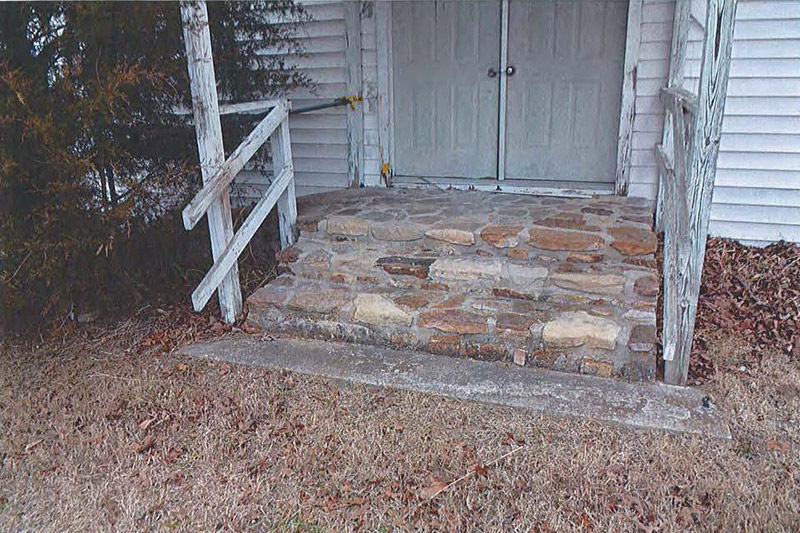 Stone steps under covered entrance with wooden railings and double doors