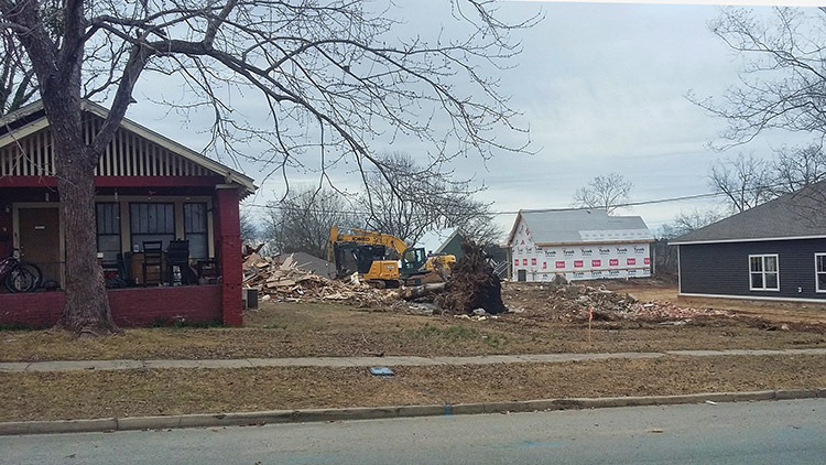 Single-story house next to demolished house and construction equipment on street
