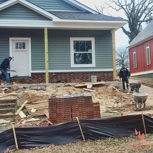 New house under construction with white men working on porch and pile of bricks near the street