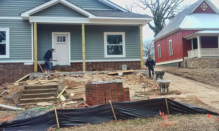 New house under construction with white men working on porch and pile of bricks near the street