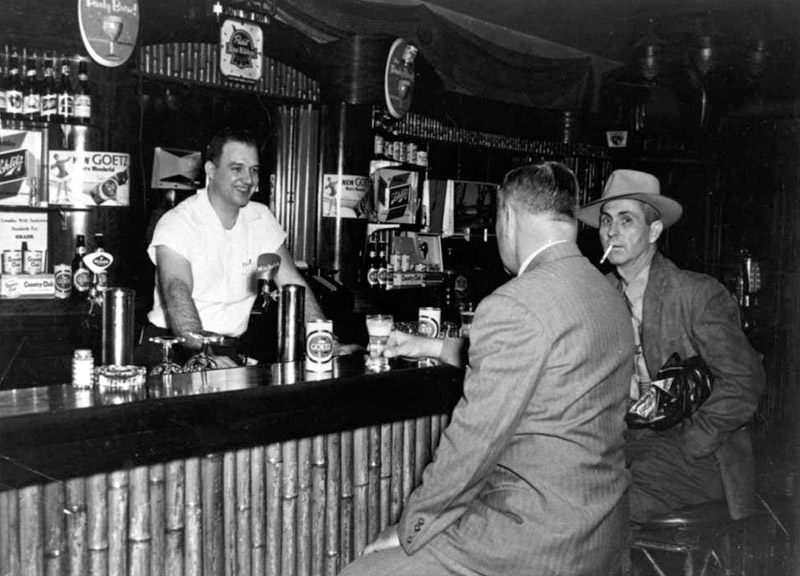 White bartender serving two white men in suits at hotel bar