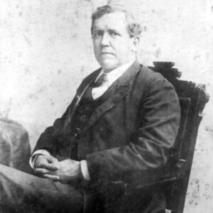 White man in three piece suit sitting in a chair with hands folded in his lap