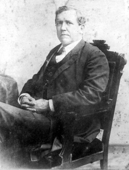White man in three piece suit sitting in a chair with hands folded in his lap