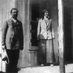 White man and white woman standing on before wooden building