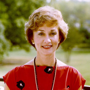 White woman smiling in red dress with bead necklaces