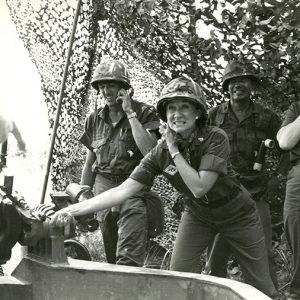 White woman in military uniform firing artillery from under canopy with other soldiers