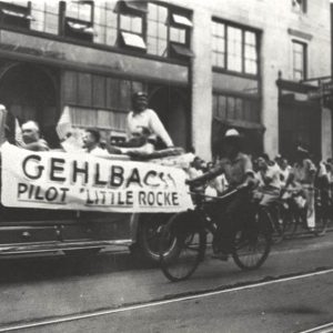 White man riding in open car in parade with spectators observing