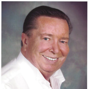 Older white man with dark hair smiling in white shirt