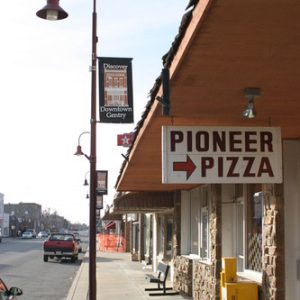 "Pioneer Pizza" sign on storefront with curved street lamp and parked cars