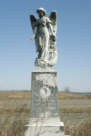 Angel statue on engraved grave monument in field