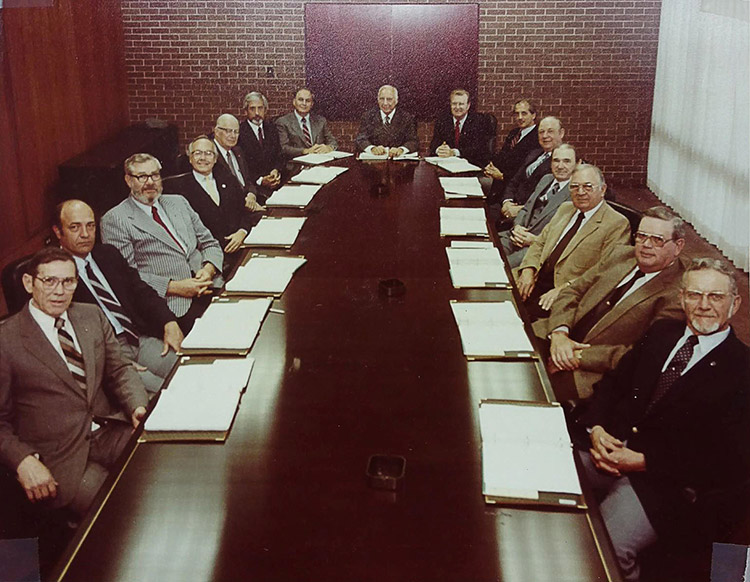Group of older white men in suits seated around a long table