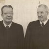 Older white man with glasses standing next to older white man with both wearing judge's robes