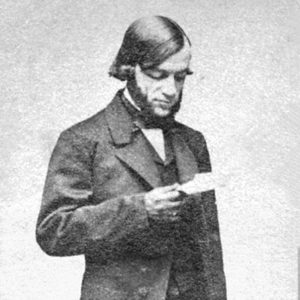 White man with sideburns in suit and bow tie reading a piece of paper