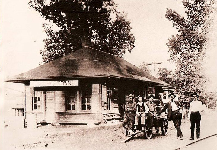 Group of men with cart outside single-story railroad building