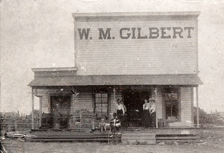 White men woman and child at "W. M. Gilbert" store on dirt road