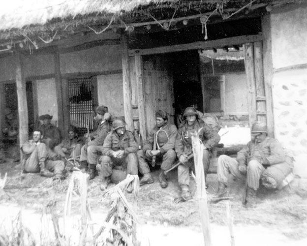 Mixed group of men in military uniforms resting outside Korean house