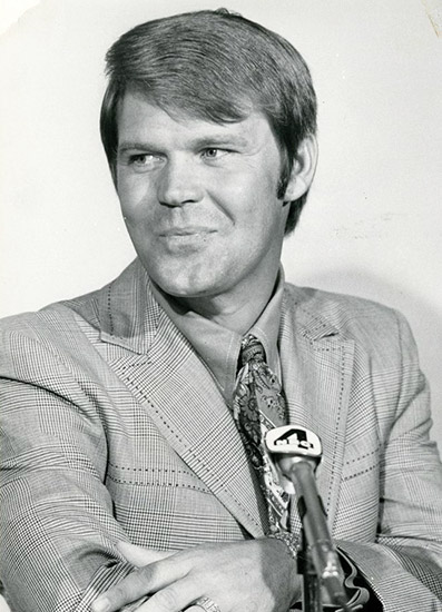White man with short hair in suit and tie in front of a microphone