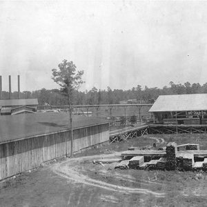 Long row building with stacks of lumber and water tower