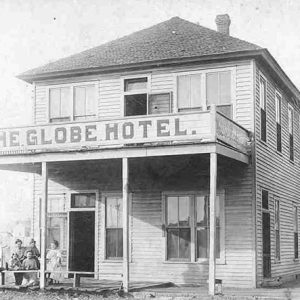 Two-story hotel building "The Globe Hotel" with white visitors and tree