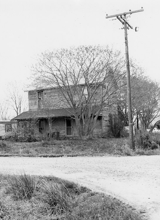 Two-story house and telephone pole on dirt road