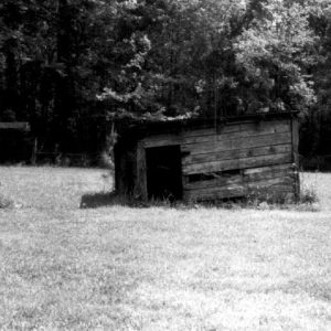 Dilapidated outbuilding with missing boards and door on grass