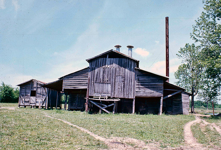Weathered barn-like building with smokestacks in field