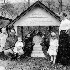 White man woman and children at grave with stone marker and covering in cemetery