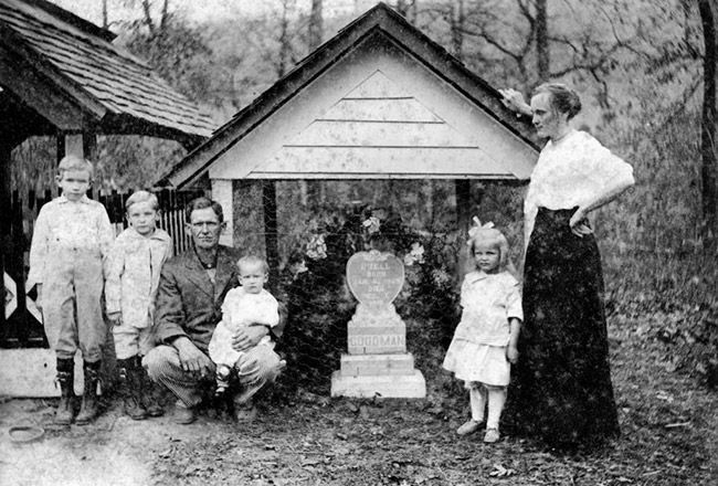 White man woman and children at grave with stone marker and covering in cemetery