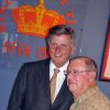 Older white man in suit and tie standing next to older white man in plaid shirt with crown "King Biscuit Time" logo on the wall behind them