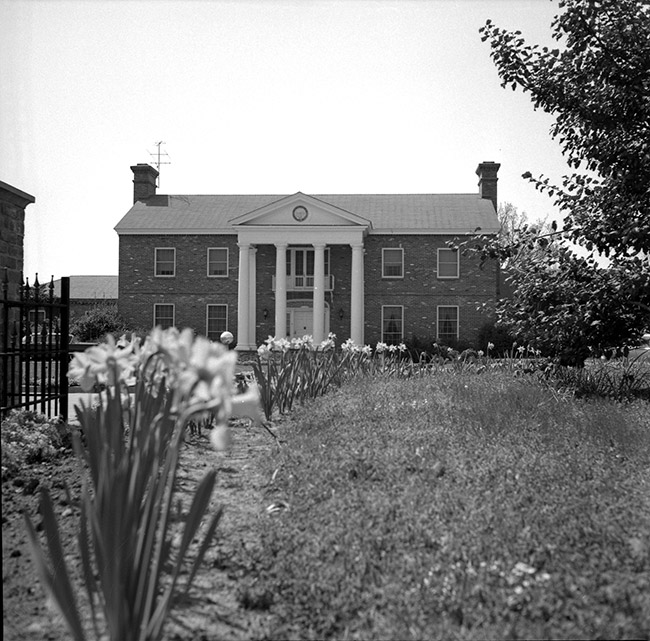 Two-story house with covered porch supported by four columns with flowers and gate in the foreground