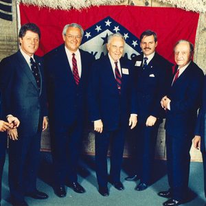 Group of white men in suits with Arkansas flag in background