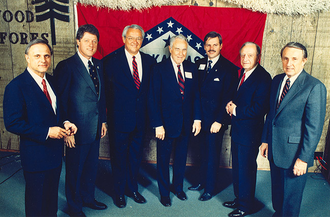 Group of white men in suits with Arkansas flag in background