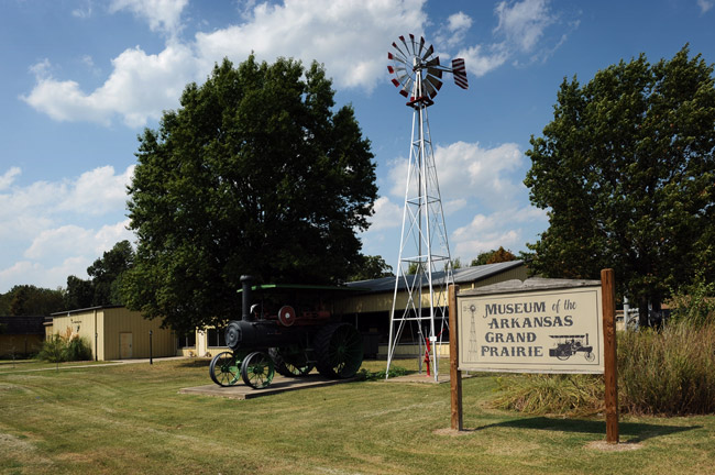 Single-story building with steam tractor on display and windmill "Museum of the Arkansas Grand Prairie"