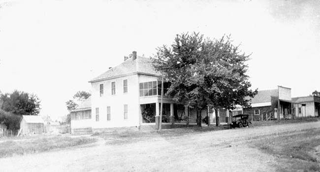 Two-story hotel building with tree on dirt road with storefronts