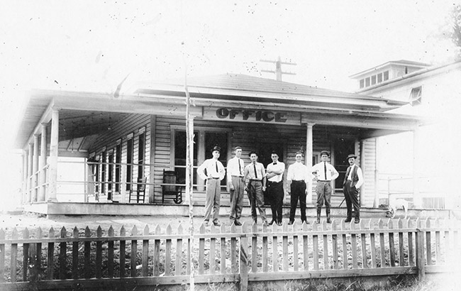 Group of white men in front of office building with fence