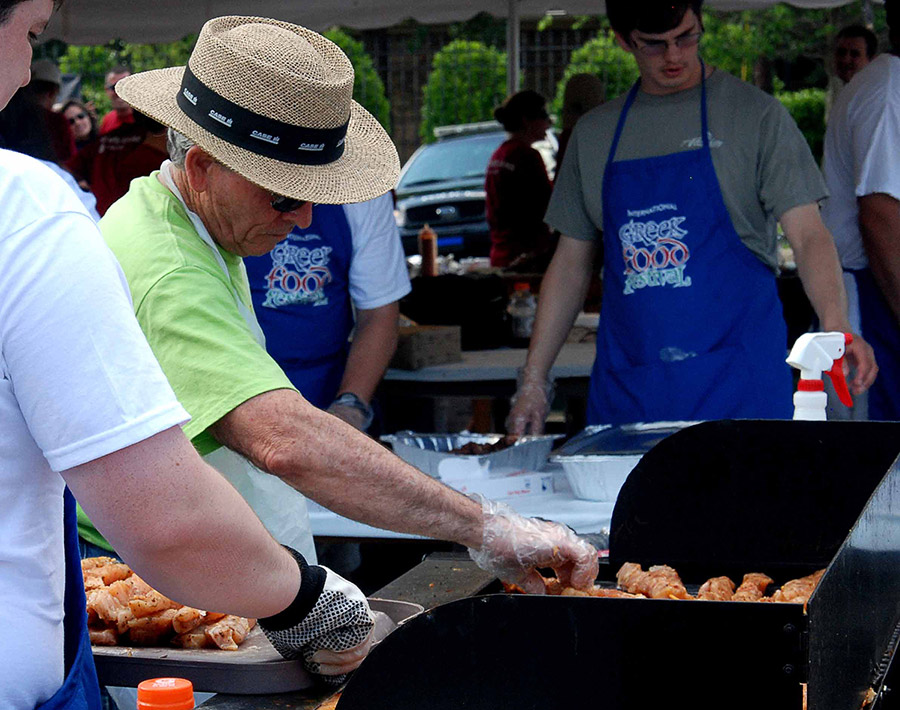 Older white man in hat and white men in blue aprons grilling  outdoors
