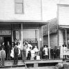 Group of white men women and children outside two-story storefront