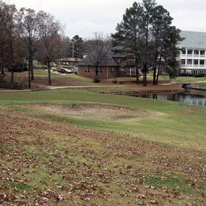 Golf course with pond trees and small brick building with cars and white building with balconies