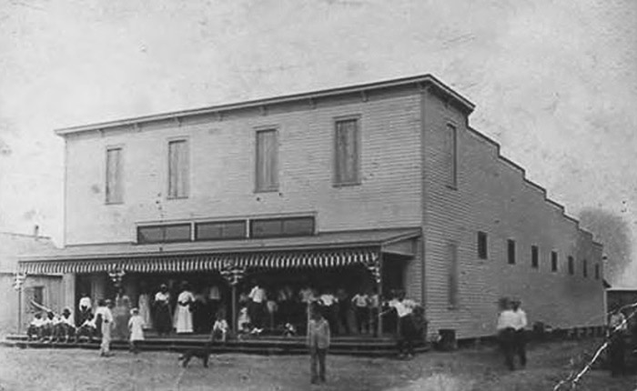 People standing in front of storefront on dirt road