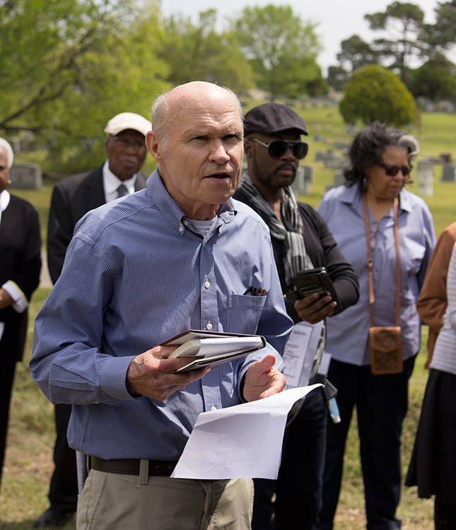 Old white man holding book and notes speaking with African-American men and women behind him