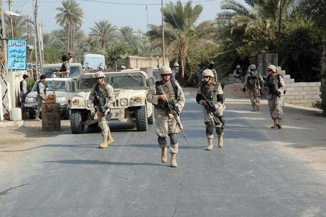 Male soldiers patrol city street with military vehicle and palm trees in background