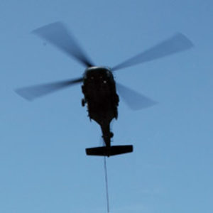 Helicopter flying with bucket on long cable releasing water