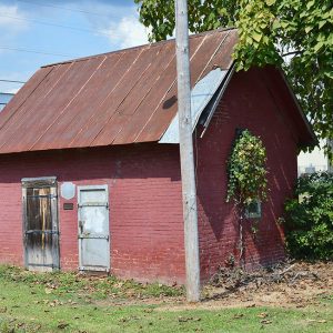 Small red brick building with two doors and rusted metal roof