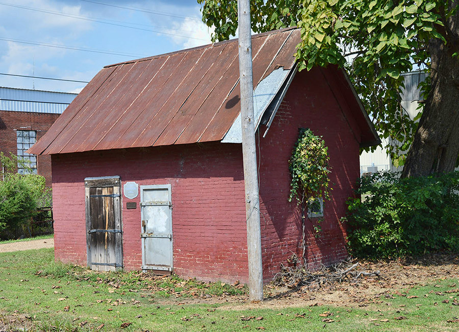 Small red brick building with two doors and rusted metal roof