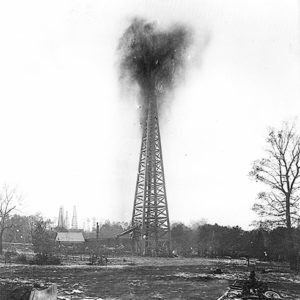 Oil gushing from a steel derrick with single-story building nearby
