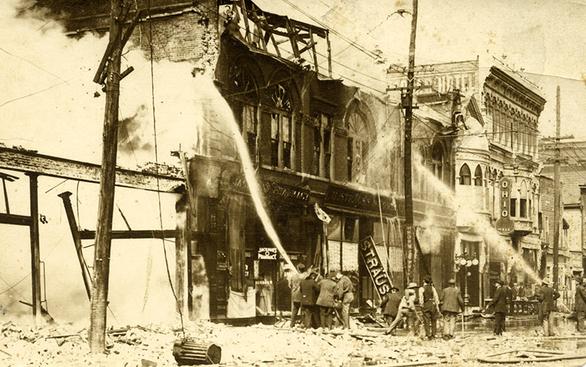 Firemen using water hoses to put out fire on row of burning buildings