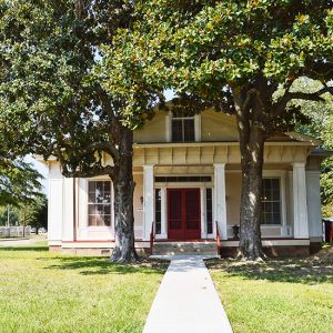 House with four porch columns red doors and sidewalk between two trees in front yard