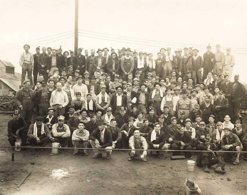 Group of men seated and standing in rows outdoors